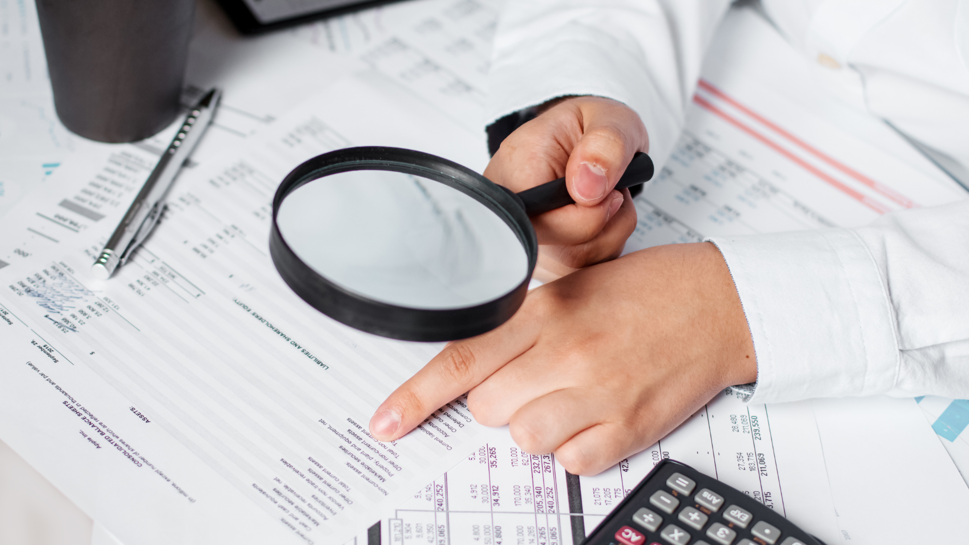 Analyse de documents financiers avec une loupe, mettant en évidence les détails, accompagnée d'un stylo et d'une calculatrice sur le bureau